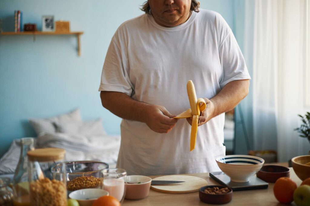 persona obesa sbuccia una banana in cucina