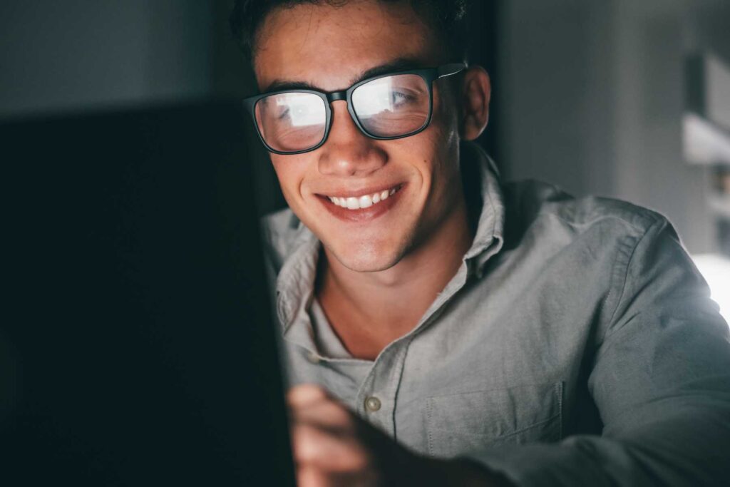 ragazzo giovane sorride dietro lo schermo del computer